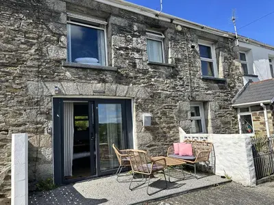 a patio with chairs and a table in front of a stone building at The Little Cottage at Porth in Newquay