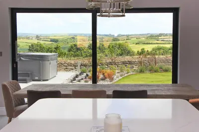 a dining room with a view of the countryside through a window at Stylish home with HOT TUB in St Merryn