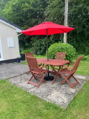 a picnic table with two chairs and a red umbrella at Beekeepers Cottage in Liskeard