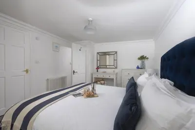 a white bedroom with a bed with a blue headboard at Mount Pleasant, St Ives in St Ives