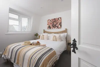 a white bedroom with a bed with a striped blanket at Mount Pleasant, St Ives in St Ives