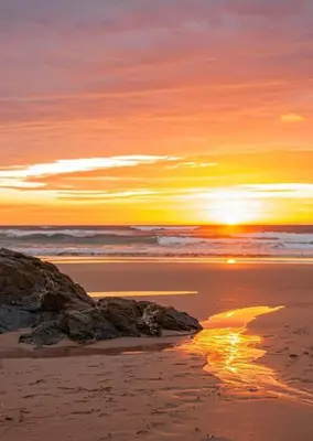 a sunset on a beach with a rock in the sand at Willow Bungalow Quiet and secluded in Carbis Bay