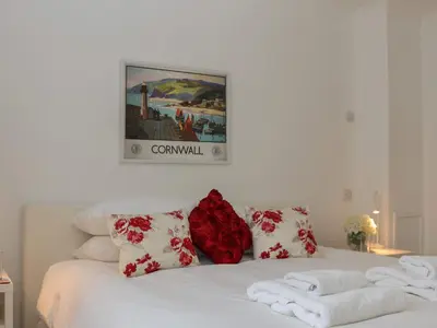 a white bed with red and white pillows and a picture at Blue Vista in Carbis Bay