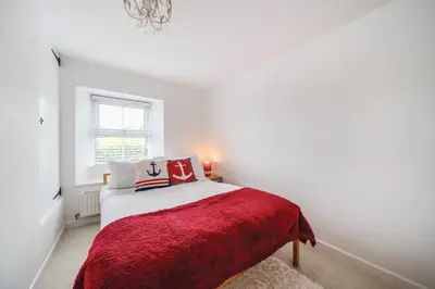 a white bedroom with a bed with a red blanket at Fowey, Cute Cottage in Fowey