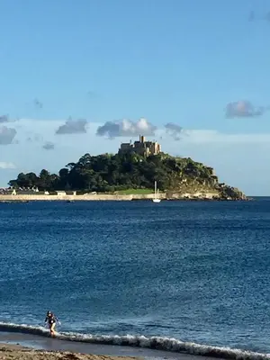 a person walking on the beach with an island in the water at Guest Room with Parking Near St Ives & Penzance in Penzance