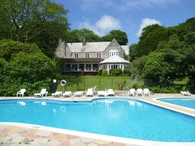 a swimming pool with chairs and a house in the background at Villa 18 Lanteglos Holiday Park in Camelford