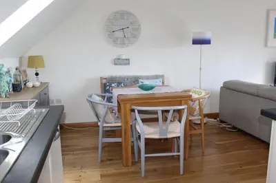 a kitchen with a table and chairs and a clock on the wall at Apartment 19 in Downderry