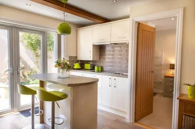 a kitchen with white cabinets and a table with green stools at Cosy Couples Getaway - The Nook, set in 6 acres of private grounds in Truro