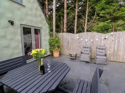 a wooden table with a vase of flowers on a patio at Little Willow in Saint Columb Major