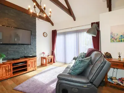a living room with a leather couch and a flat screen tv at The Stables in Saint Columb Major
