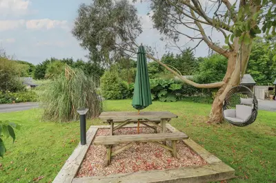a picnic table with a green umbrella next to a tree at The Stables in Saint Columb Major