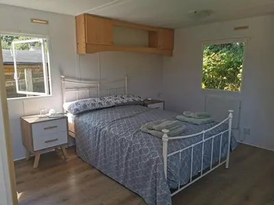a bedroom with a bed and a nightstand and two windows at Meadow Bluebird in Bodmin