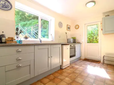 a kitchen with white cabinets and a window at Jordan Cottage in Fowey