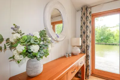a vase with flowers on a wooden table with a mirror at 10 Water's Edge in Looe