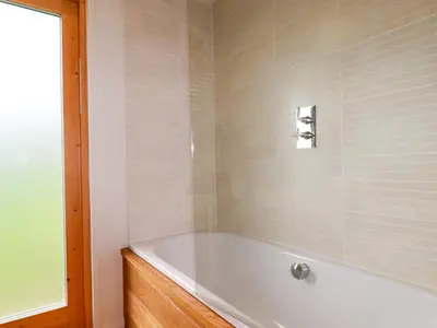 a bath tub in a bathroom with white tiles at 1 Hedgerows in Looe