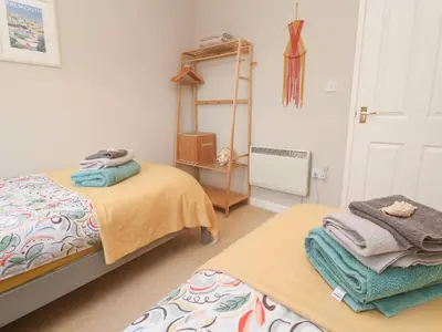 a bedroom with two beds and a shelf with towels at Jaspers Retreat, formerly known as Starfish Cottage in Falmouth