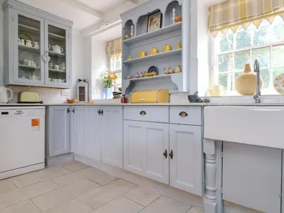 a kitchen with white cabinets and blue shelves at Connie's Cottage in Helston