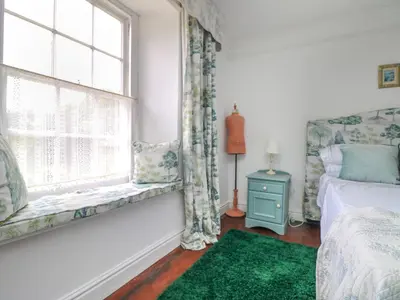 a bedroom with a bed and a window with a green rug at Connie's Cottage in Helston