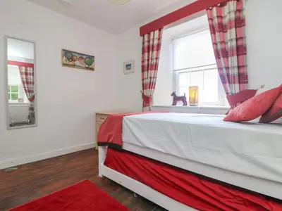 a bedroom with a bed with a red blanket and a window at Connie's Cottage in Helston