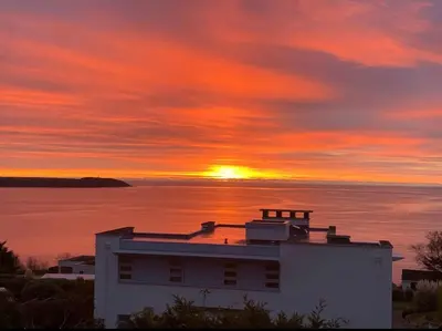a sunset over a house with the ocean in the background at Harber Rise House in Carlyon Bay