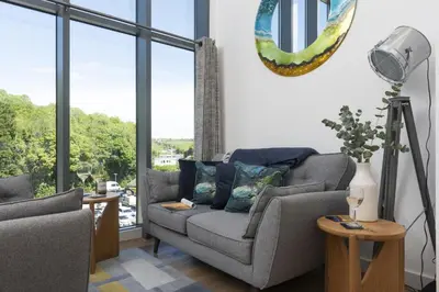 a living room with a couch and some windows at Landing View Fowey Penthouse in Fowey