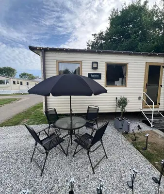 a table and chairs with an umbrella in front of a trailer at Cornwall caravan in Crantock
