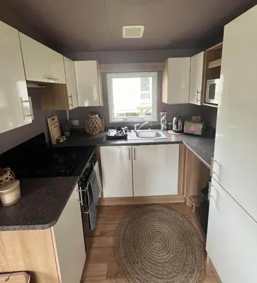 a kitchen with white cabinets and a sink and a window at Cornwall caravan in Crantock
