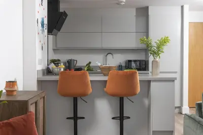 a kitchen with a counter with two orange bar stools at Sea Breeze, Newquay in Newquay