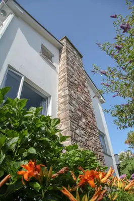 a brick chimney on a white house with flowers at Birdsong in Carbis Bay