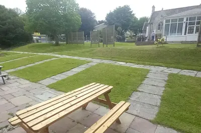 a wooden bench sitting in the grass near a park at Sunny holiday house in Newquay