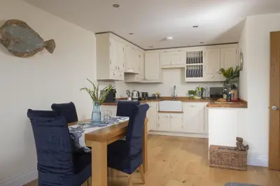 a kitchen with white cabinets and a table and chairs at 5 Sandy Lane Apartments, Carbis Bay in Carbis Bay