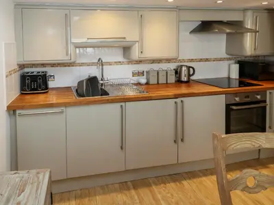 a kitchen with white cabinets and a wooden counter top at Cormorant Cottage in St Ives
