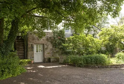 a stone house with a white door and trees at The Watermill in Bodmin