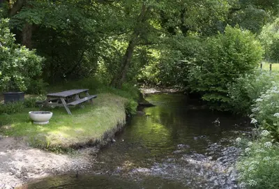 a picnic table next to a stream with a stream at The Watermill in Bodmin