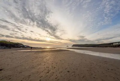 a person standing on a sandy beach with a cloudy sky at Stradav in Polzeath