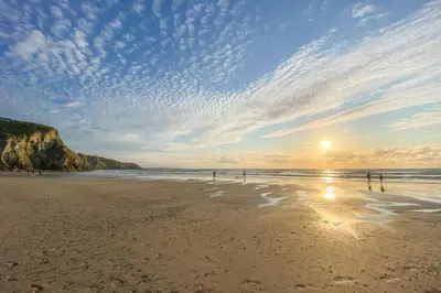 a beach with the sun shining on the sand at Castaways in Porthtowan