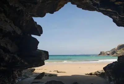 a view of the beach through a rock formation at Bowjy Cottage in St. Agnes