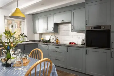 a kitchen with gray cabinets and a table with a dining room at Bowjy Cottage in St. Agnes