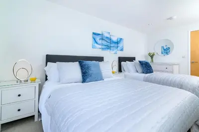 two beds in a white bedroom with blue accents at The Penthouse, 48 Zinc in Newquay