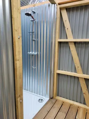 a shower in a corrugatedsteel walled shower with a shower head at Tylda Tents at Tregonetha Lake - 5m Luxury Bell Tent 