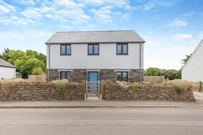 a white house with a stone wall and a blue door at 4 Bed in Windmill oc-w29654 in St Merryn