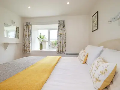 a bedroom with a large white bed and a window at Bray Cottage in Bodmin
