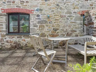 two chairs and a table in front of a stone wall at Bray Cottage in Bodmin