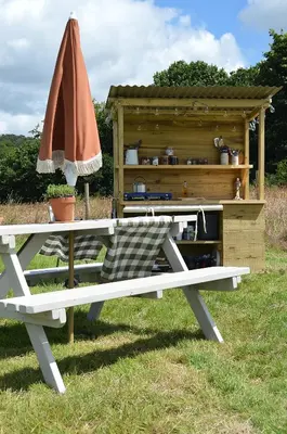 a picnic table with an umbrella next to a wooden shed at Tylda Tents at Heydaze Campsite - 5m Luxury Bell Tent 