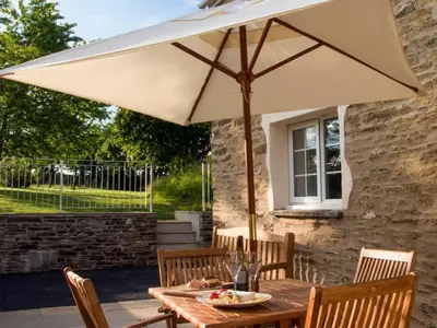 a wooden table with an umbrella on a patio at Penny's Cottage-Uk12572 in Bodinnick
