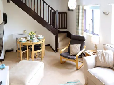 a living room with a table and a stairway at April Cottage in Padstow
