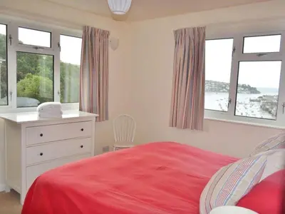 a bedroom with a red bed and a dresser and windows at Harbourside in Fowey