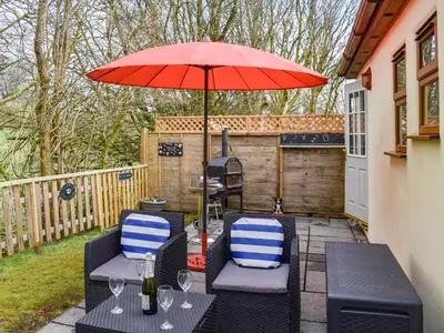 a patio with two chairs and an umbrella at 15 Pebble Cottage in Camelford