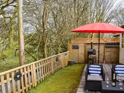 a patio with two chairs and a red umbrella at 15 Pebble Cottage in Camelford