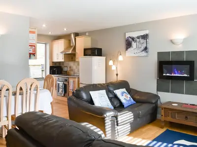 a living room with a leather couch and a kitchen at 15 Pebble Cottage in Camelford